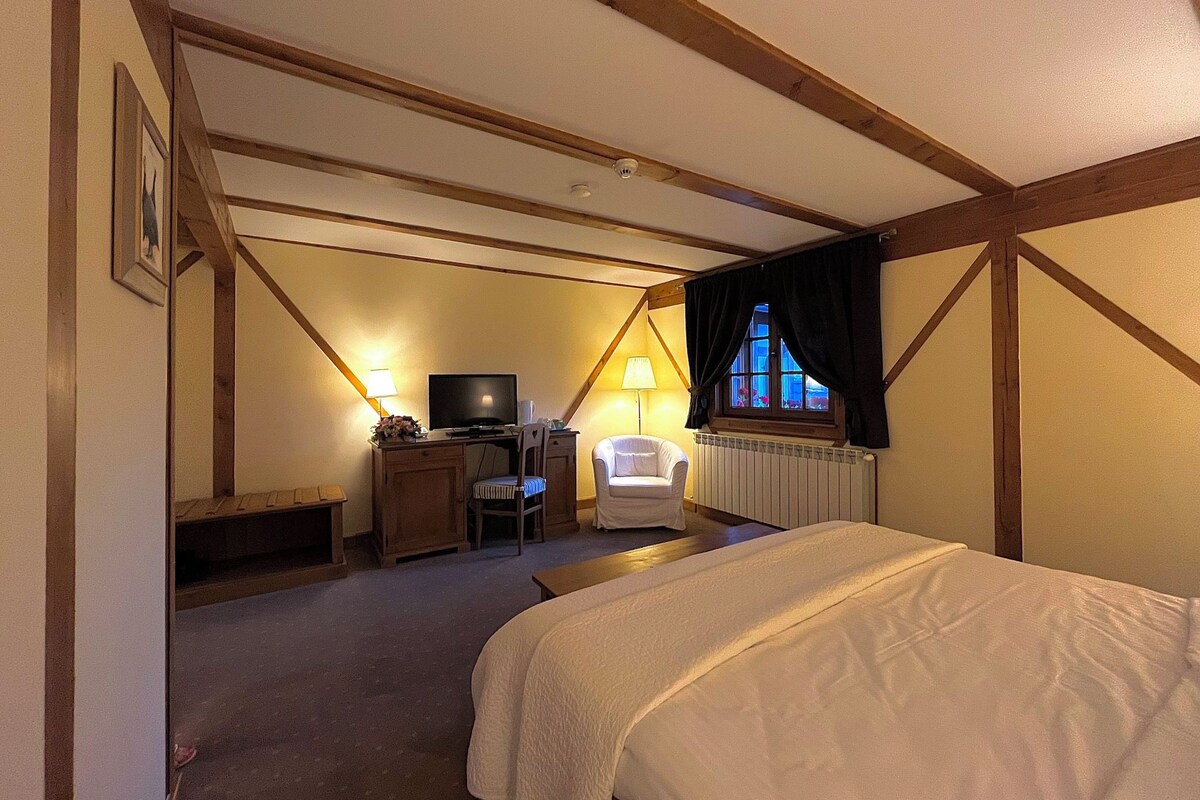 Un dormitorio con cama, escritorio con computadora, silla y ventana con cortinas.