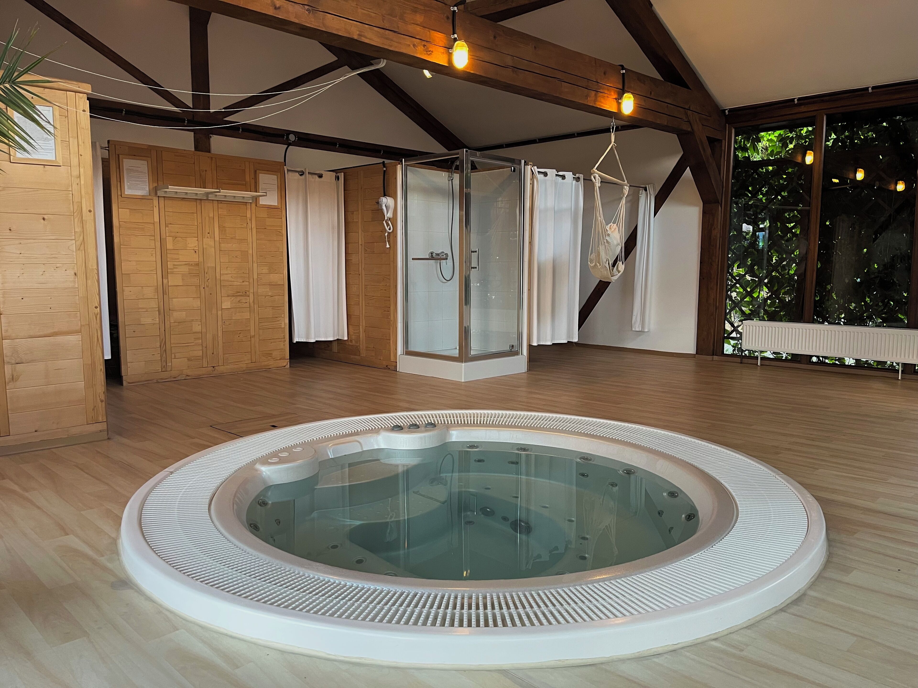 Un cuarto de spa con hidromasaje, paredes de madera, cabina de ducha de vidrio y vistas a la vegetación exterior.