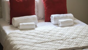 Un lit bien fait, avec une couette blanche matelassée, deux oreillers rouges et deux serviettes blanches roulées.