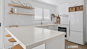 A modern kitchen with white cabinetry, a central island with stools, a built-in oven, and a refrigerator. - Castaway, Cowes beach house (Cowes)