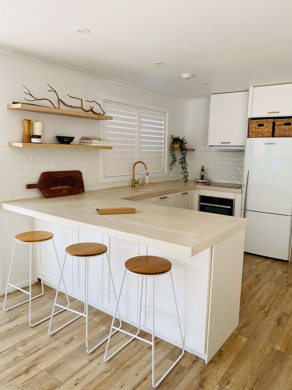 A modern kitchen with a central island, white cabinetry, and a built-in oven. - Castaway, Cowes beach house (Cowes)