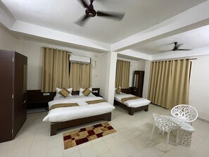 A hotel room with two beds, a ceiling fan, a small white chair, and a checkered rug. - Erica Residency (Guwahati)
