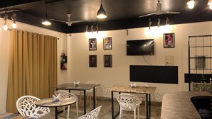 Una stanza con soffitto nero, sedie bianche, un tavolo, una TV a parete e una tenda a sinistra.