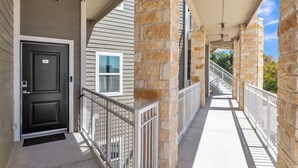 A covered outdoor corridor with stone pillars, a black door labeled '204', and a white railing. - Walk to Gruene-Guadalupe Riverfront-River Access-Stylish Texas Music Retreat (New Braunfels)