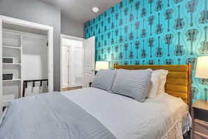 A bedroom with a bed, a wardrobe, a nightstand, and a wall with a guitar pattern.
