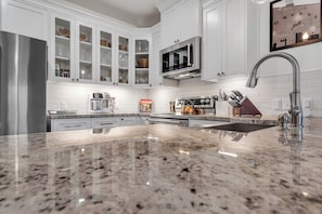 A modern kitchen with white cabinets, a stainless steel refrigerator, a microwave, and a granite countertop. - Walk to Gruene-River Access-Stylish Texas Retreat (New Braunfels)