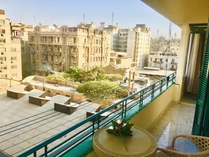 Varanda com vista para a paisagem urbana, uma pequena mesa com uma flor e uma cadeira.
