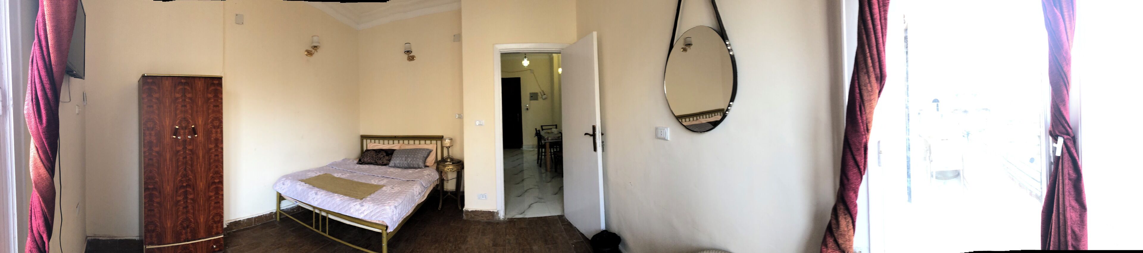 A bedroom with a bed, a wardrobe, a mirror, and a door leading to another room.