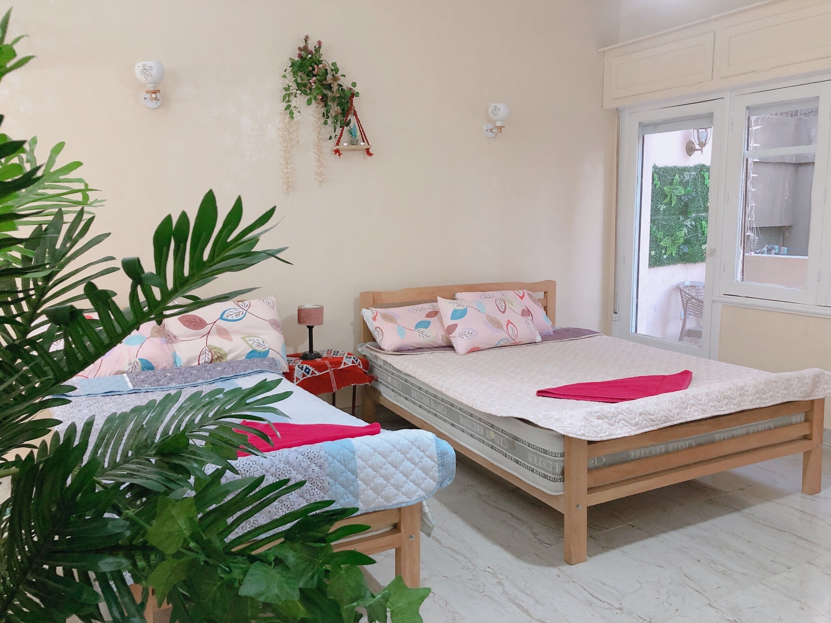 Une chambre avec deux lits, une fenêtre et une plante fixée au mur.