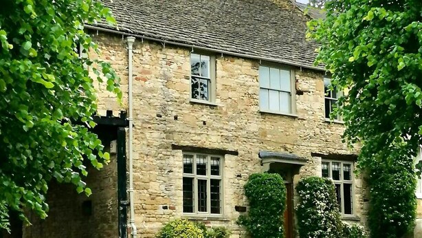 A stone building with a traditional design, featuring a central entrance, windows, and a paved driveway. - Ostlers - beautiful former Coaching Inn with parking and late Sunday checkout. (BURFORD)
