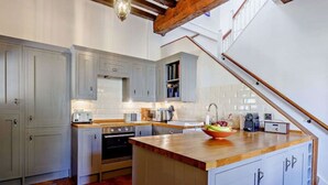 A kitchen with grey cabinets, a wooden countertop, and a central island with a sink and fruit bowl. - Ostlers - beautiful former Coaching Inn with parking and late Sunday checkout. (BURFORD)