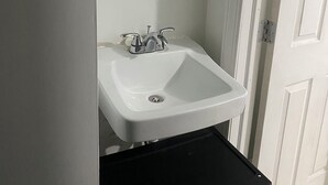 A bathroom with a white sink, a mirror above it, and a black trash bin below.