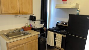 A compact kitchen with wooden cabinets, a stainless steel sink, a microwave, a stove, and a black refrigerator.