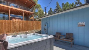 A hot tub with a wooden deck and a blue wall with a sign indicating spa hours.