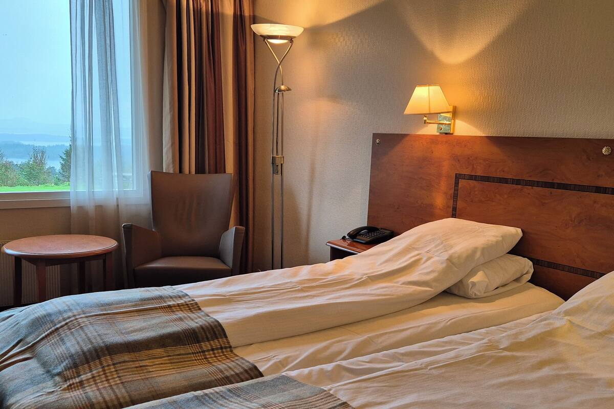 A hotel room with a bed, a chair, a small table, a lamp, and a phone on the nightstand.