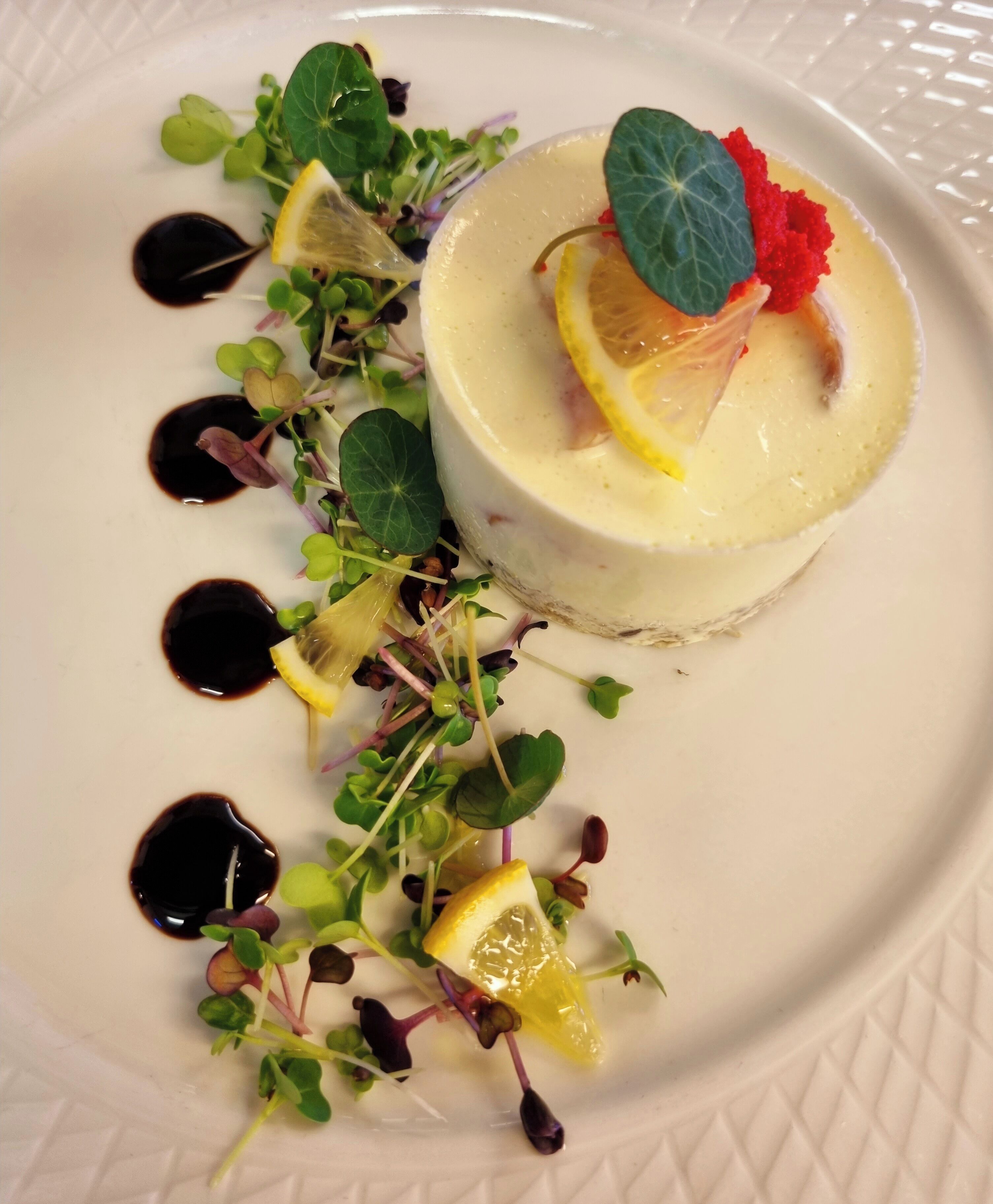 A dessert with a creamy base, lemon slices, and a red berry garnish on a white plate.