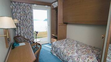 Habitación compacta con cama, escritorio, silla y una pequeña mesa. Tiene una ventana con cortinas, una puerta y vistas al exterior.