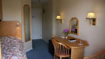 Hotellihuone, jossa on sänky, työpöytä, tuoli, peili ja kaksi seinälle asennettua lamppua.