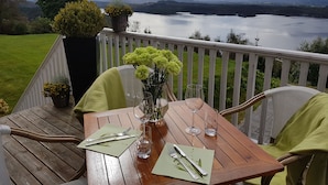 Una terraza de madera con una mesa dispuesta para dos, con vista a un lago y montañas.