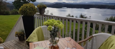 A wooden deck with a table set for two, overlooking a lake and mountains.