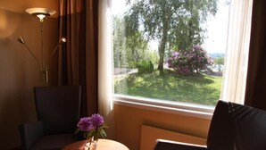 Una habitación con una mesa redonda, dos sillas, una lámpara de pie y una ventana que da a vista de árboles y flores.
