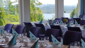 Un comedor con mesas dispuestas para una comida, sillas y vistas a un lago y montañas.