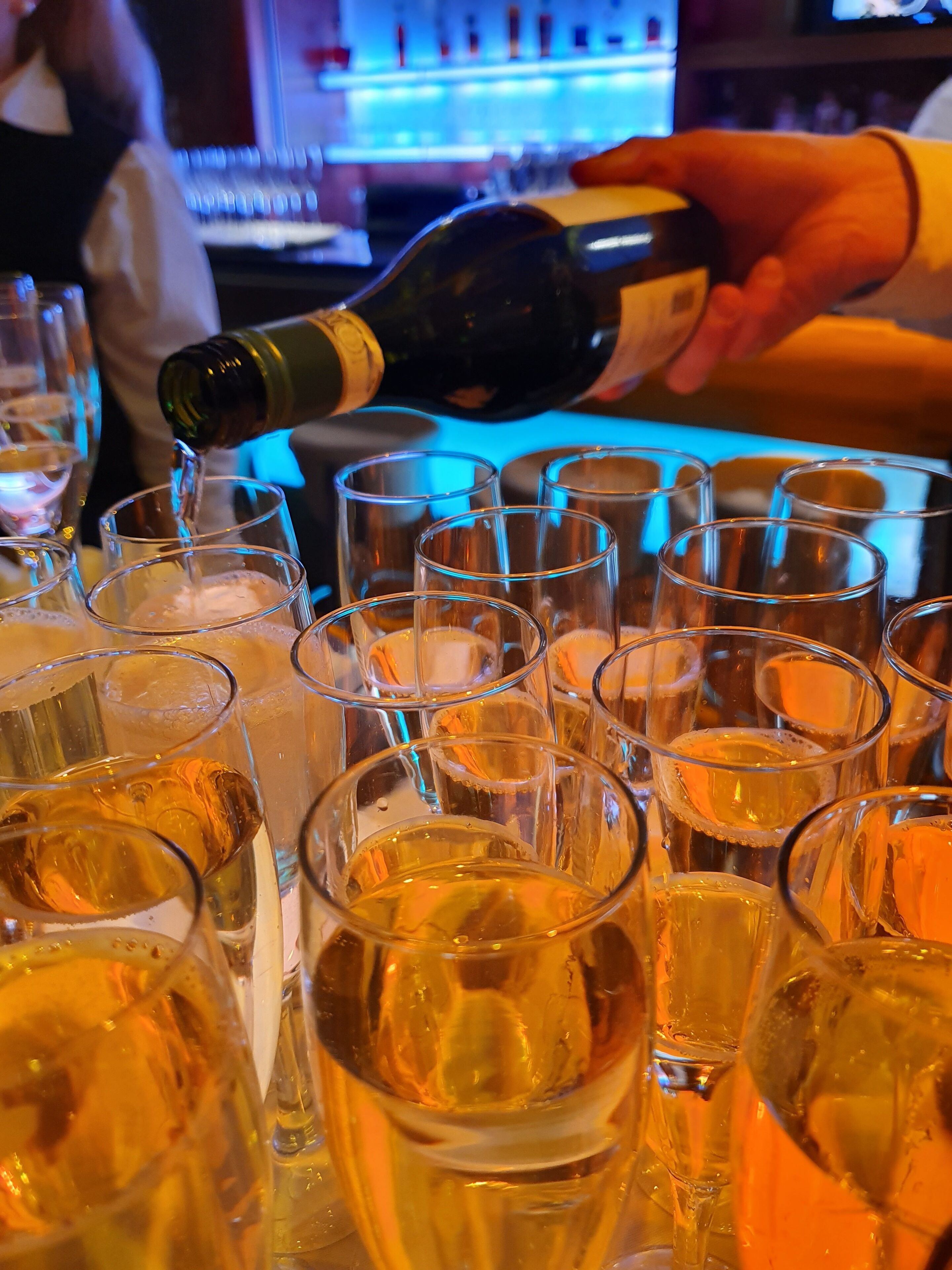 A bar setting with multiple glasses filled with a golden liquid, likely champagne, being poured.