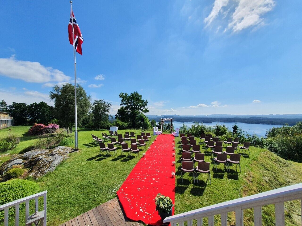 Montaje para una ceremonia de boda con alfombra roja, sillas y asta de bandera.