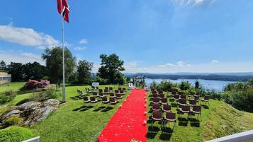 Montaje para una ceremonia de boda con alfombra roja, sillas y asta de bandera.