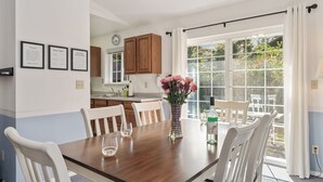 Un comedor con una mesa de madera, sillas blancas y un jarrón de flores.