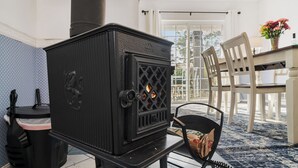 Una habitación con un estufa de leña negra, una mesa de comedor con sillas y un ventanal con cortinas.