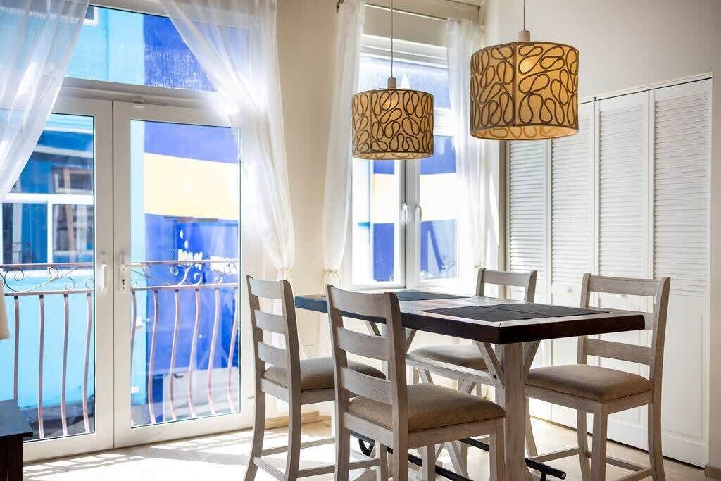 Un comedor con mesa y sillas, un balcón con barandilla y dos lámparas colgantes.