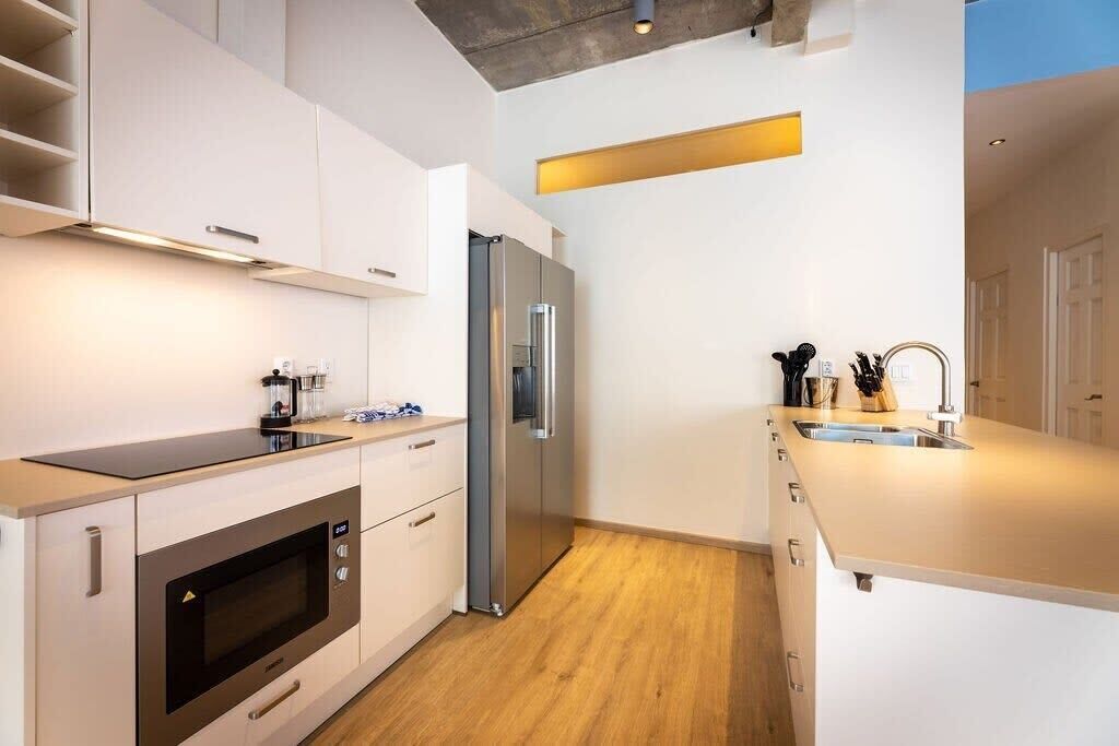Een moderne keuken met witte kasten, een roestvrijstalen koelkast, een inbouwoven en een houten vloer.