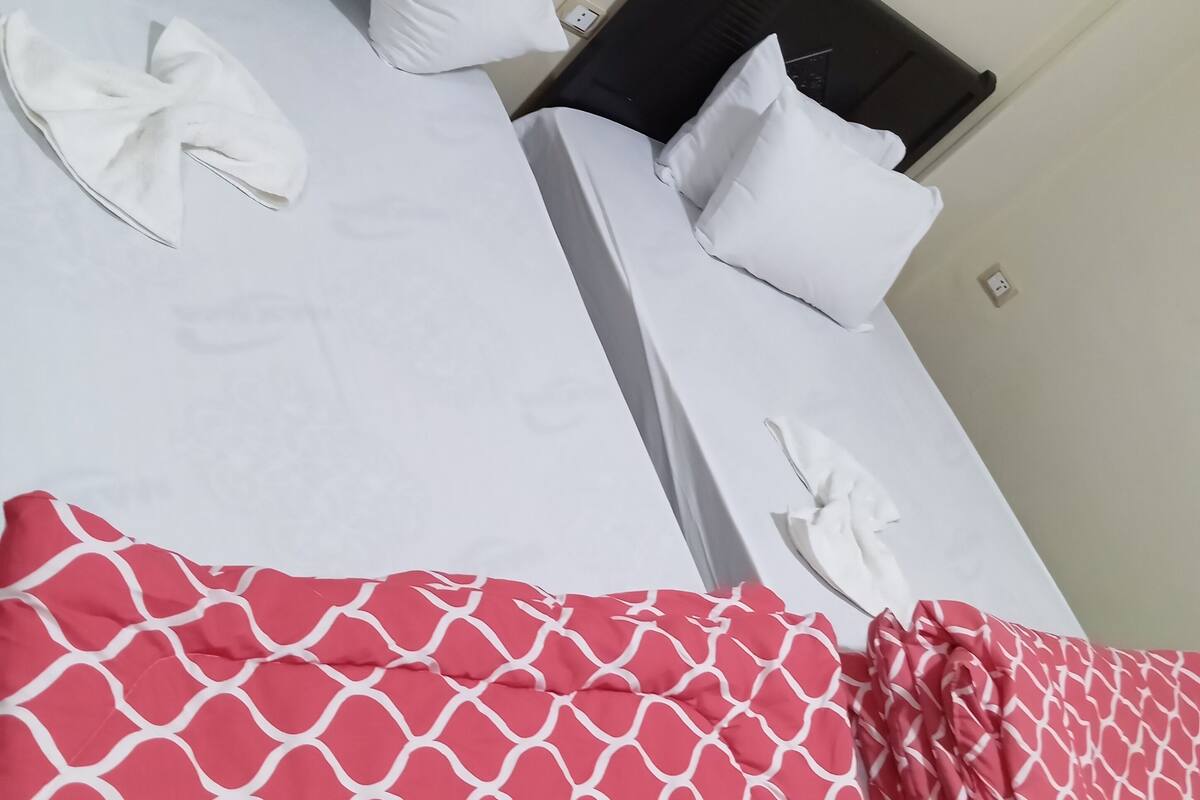 A hotel room with two beds, white bedding, and a red patterned bedspread.