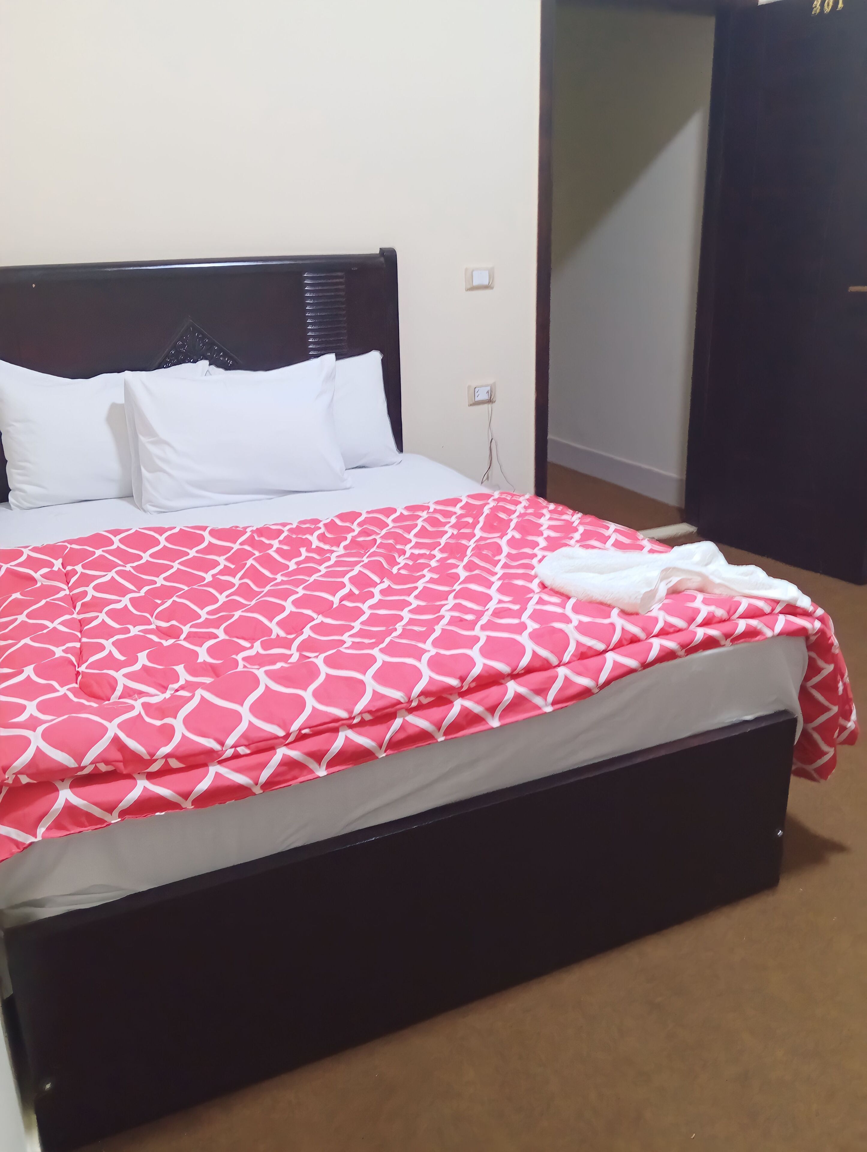 Una cama con colcha blanca y roja estampada, almohadas blancas y cabecera oscura.