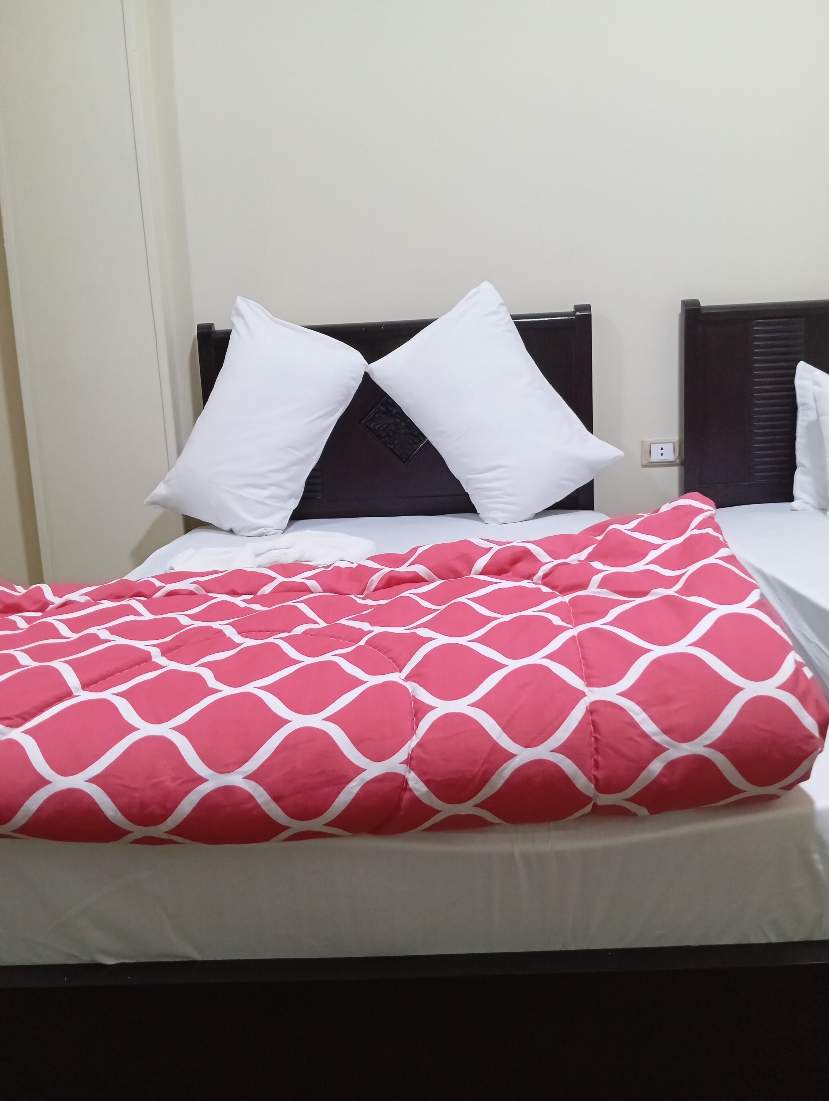 A bed with a white headboard, two white pillows, and a red and white patterned blanket.