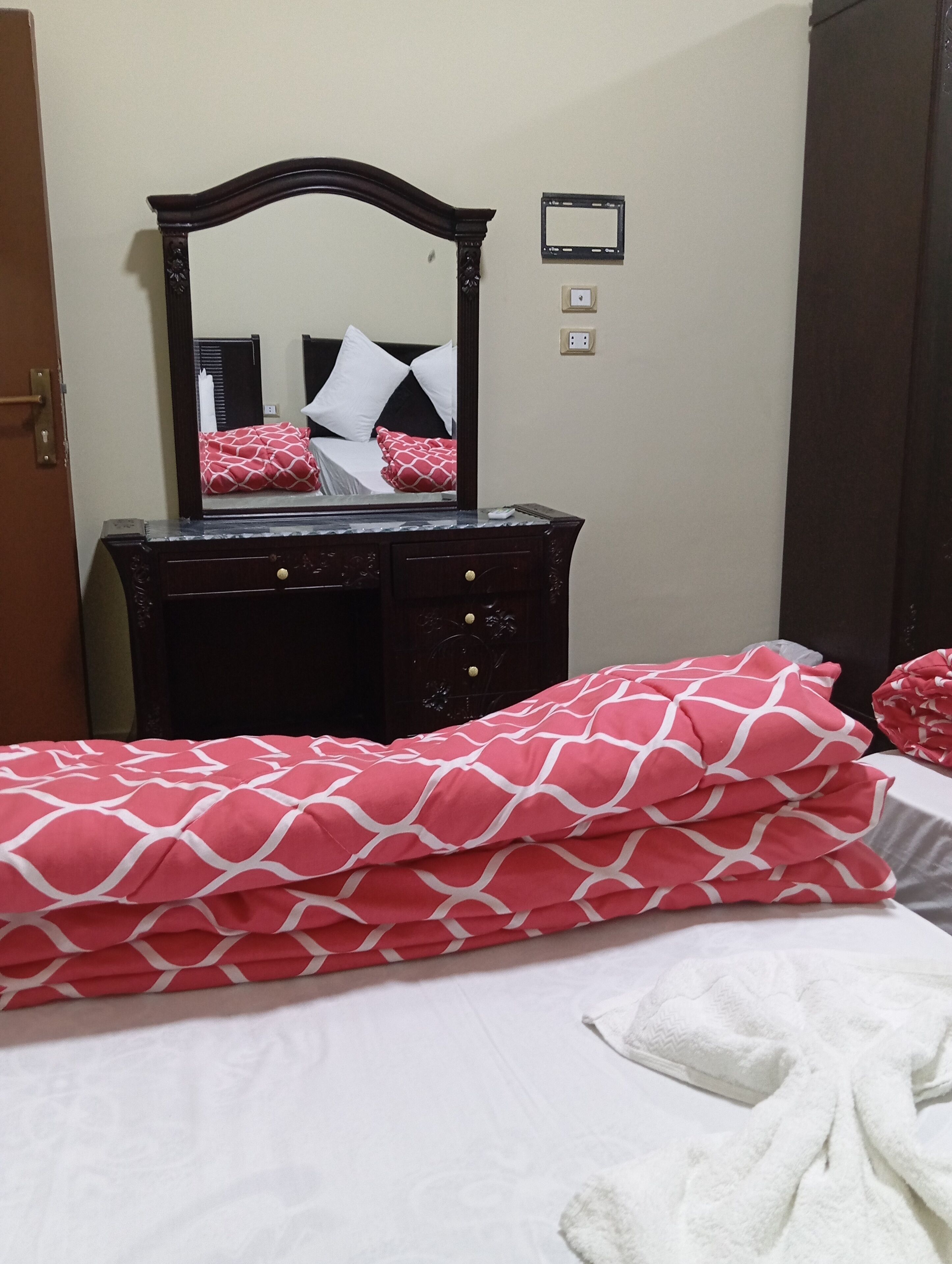 A bedroom with a bed, a dresser with a mirror, and a red patterned blanket.