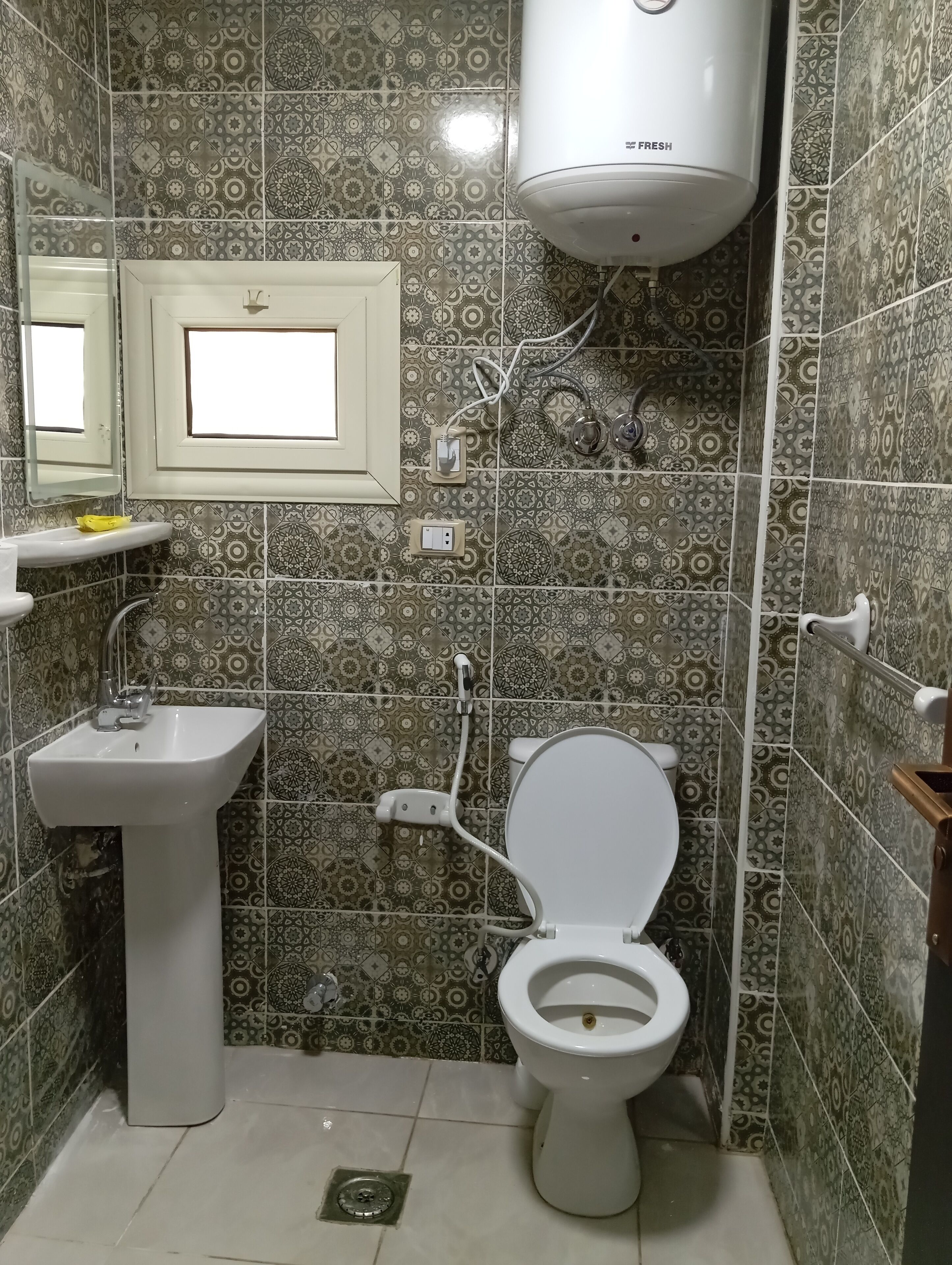 Un baño con baldosas estampadas, un lavamanos pedestal, un inodoro y un aire acondicionado de pared.