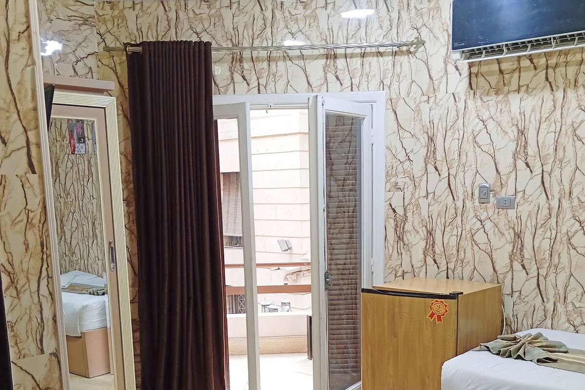 A hotel room with a bed, a wooden cabinet, a mirror, and a sliding glass door leading to an outdoor area.