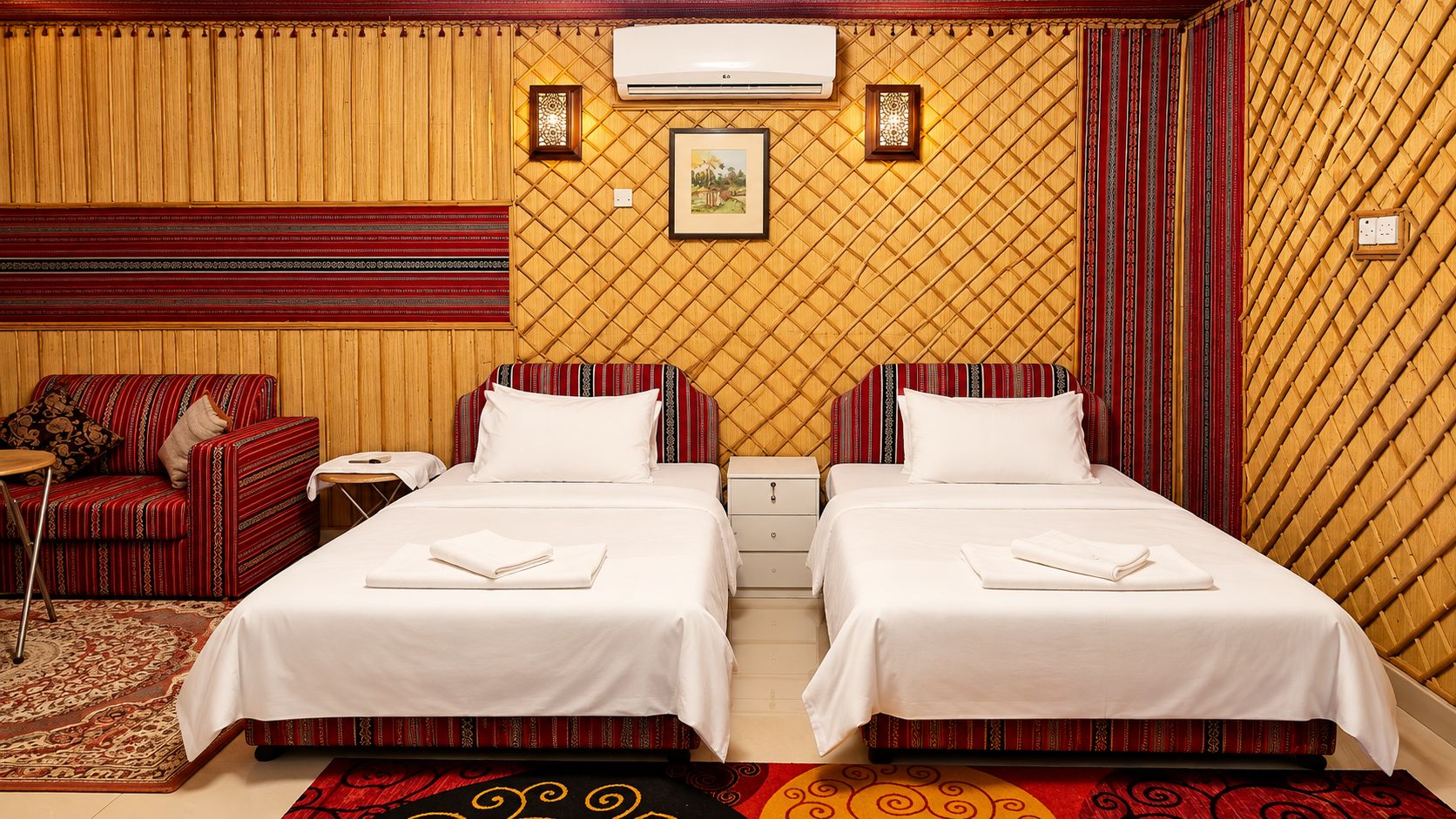 A hotel room with two beds, a sofa, a nightstand, an air conditioner, and a patterned wall.