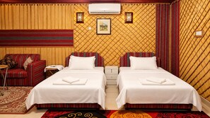 Habitación de hotel con dos camas, un sofá, una mesita de noche, aire acondicionado y pared con diseño.