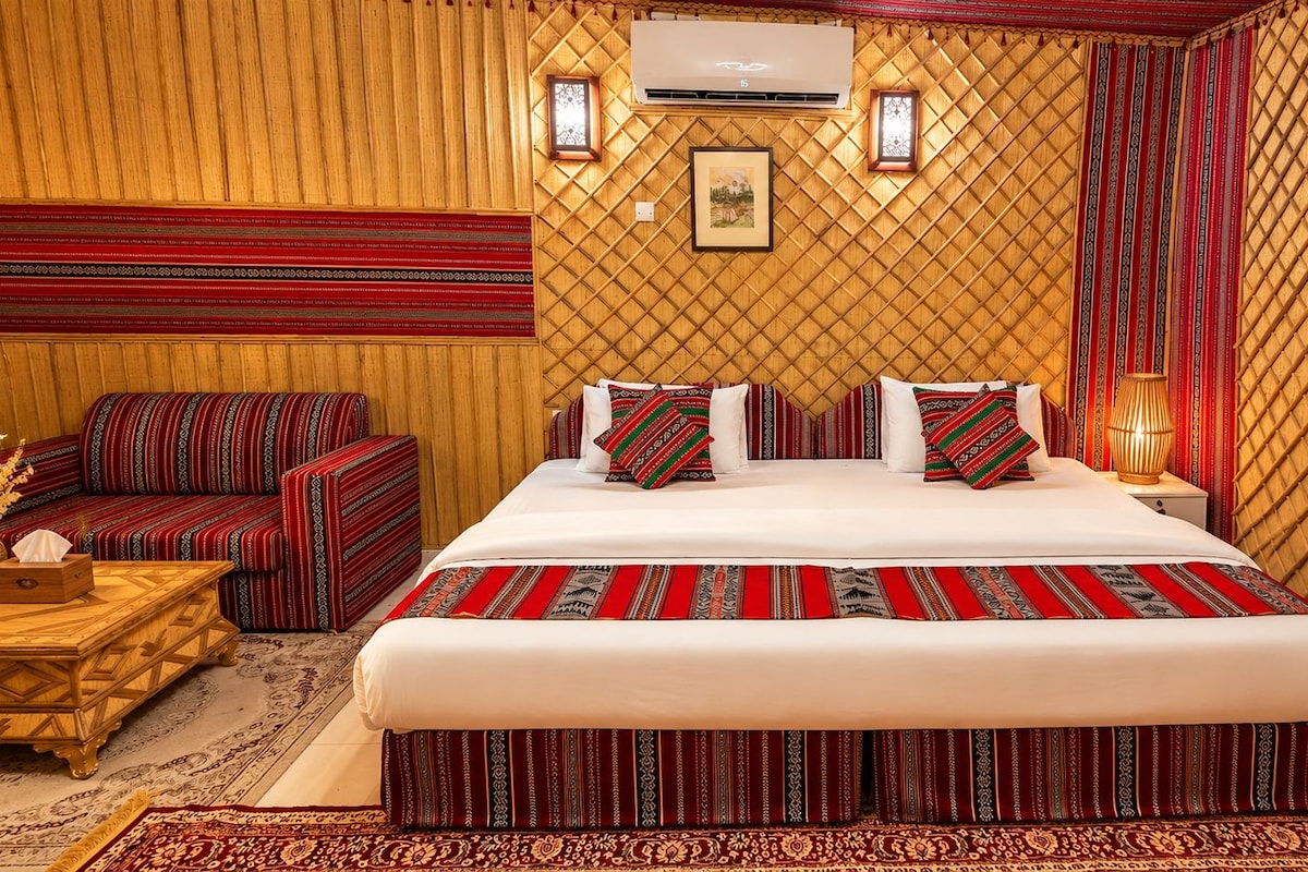 A hotel room with a large bed, a sofa, a wooden coffee table, and a patterned rug.