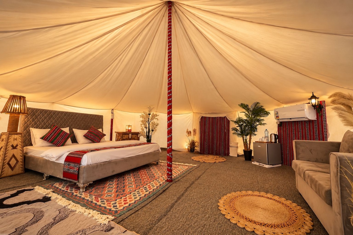 A tented room with a bed, sofa, and a small table with a lamp.