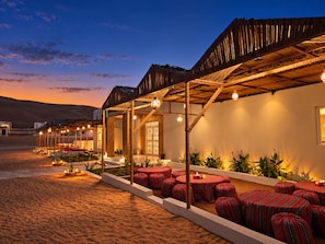 An outdoor seating area with tables and chairs, a covered structure, and a view of the desert landscape. - Al Salam Camp (Bidiya)