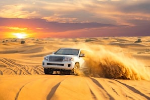 A white SUV driving through sand dunes with a sunset in the background. - Al Salam Camp (Bidiya)
