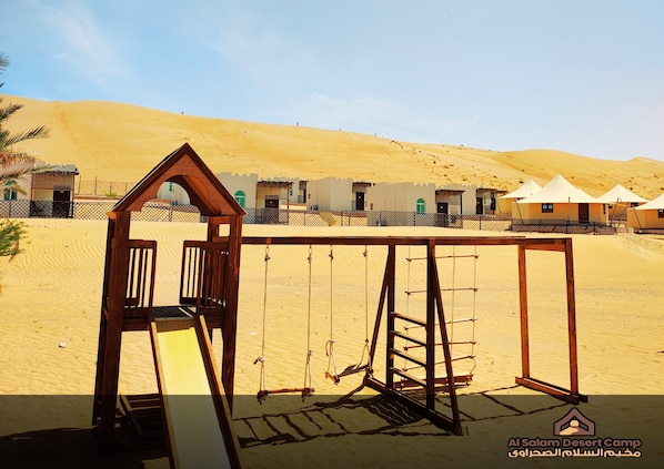 A desert camp with a wooden swing set, tents, and a fenced area. - Al Salam Camp (Bidiya)