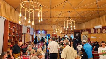 A crowded indoor dining area with wooden walls and ceiling, multiple hanging light fixtures, and a buffet setup.