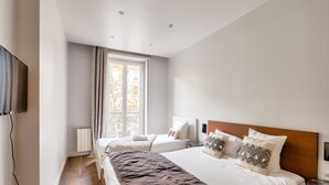 Una habitación de hotel moderna con una cama grande, televisión y ventana con cortinas.