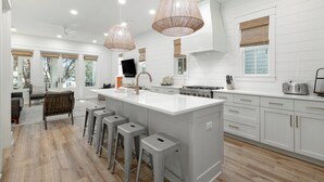 A modern kitchen with a large island, bar stools, and pendant lighting. - Watersound on 30A- Golf Cart, Pet-Friendly, Bikes (Santa Rosa Beach)