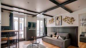 A modern living room with a grey sofa, a TV, and a dining area with chairs and a table.